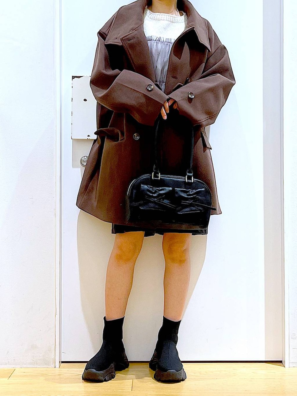 ブラウン系のステンカラーコート、ブラック系のハンドバッグ、ブラック系のブーツを着用したレディースの冬コーディネートの6枚目の写真