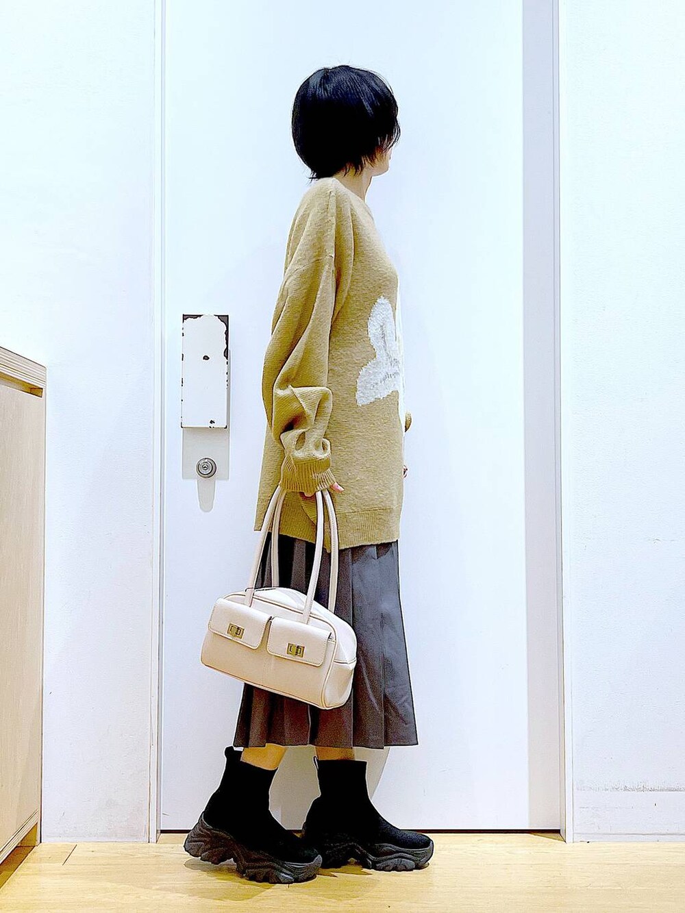 ホワイト系のハンドバッグ、ブラック系のブーツ、グレー系のスカートを着用したレディースの冬コーディネートの4枚目の写真