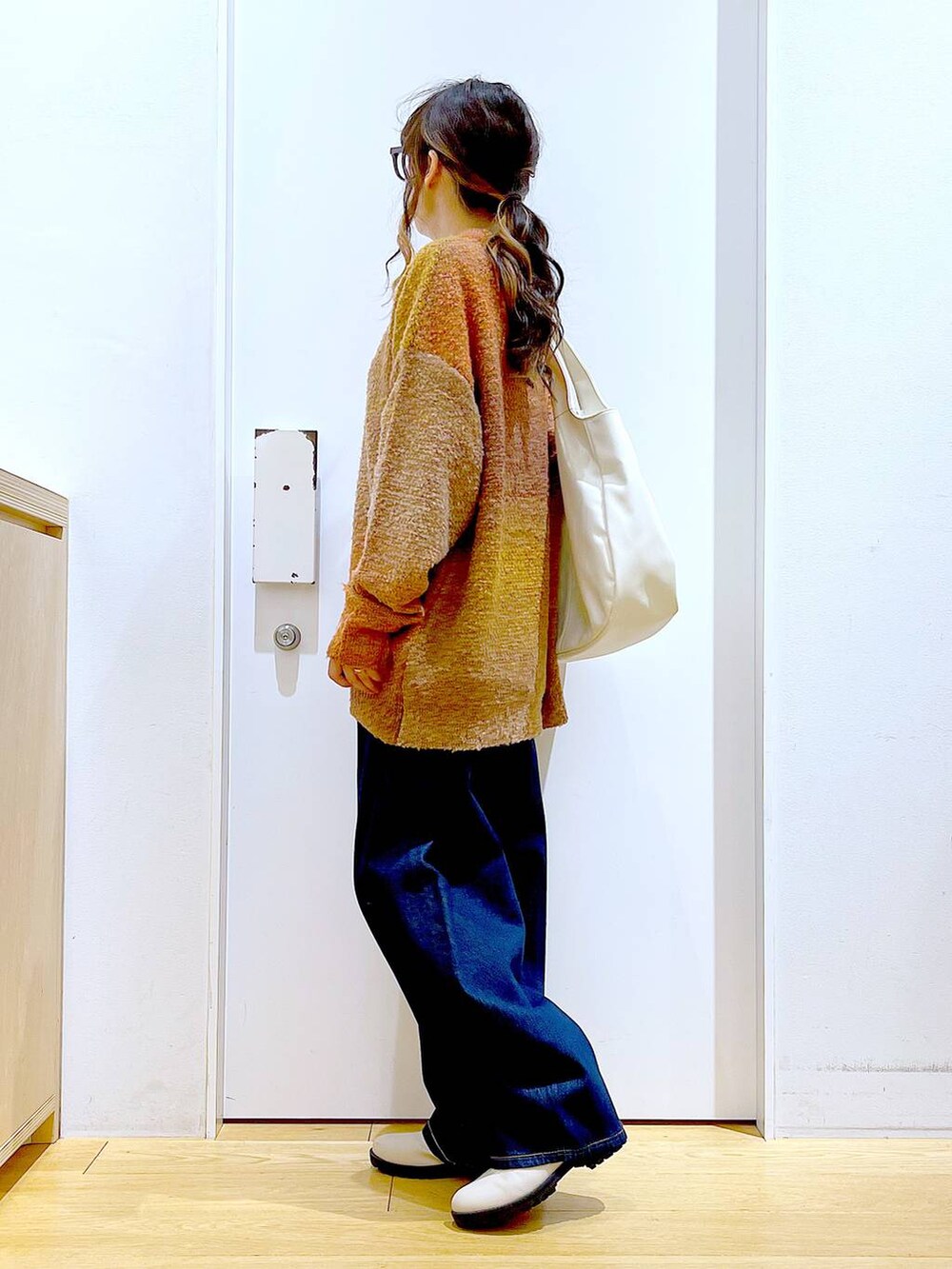 オレンジ系のニット/セーター、ホワイト系のトートバッグ、ベージュ系のブーツを着用したレディースの冬コーディネートの3枚目の写真