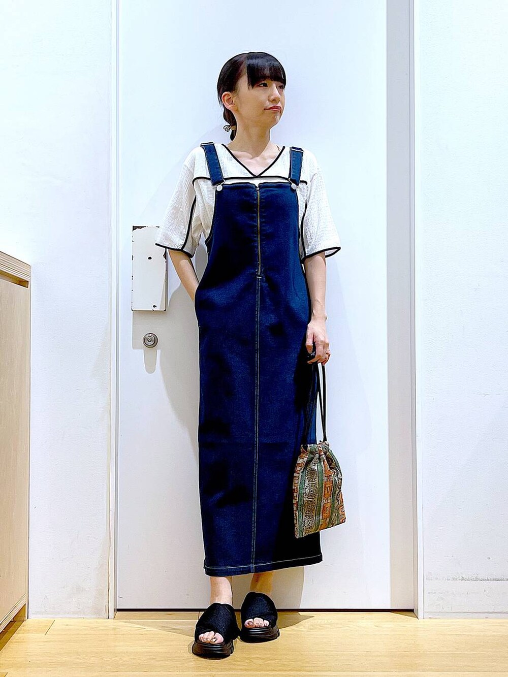 ブルー系のジャンパースカート、ブラウン系のショルダーバッグ、ブラック系のサンダルを着用したレディースの夏コーディネートの2枚目の写真