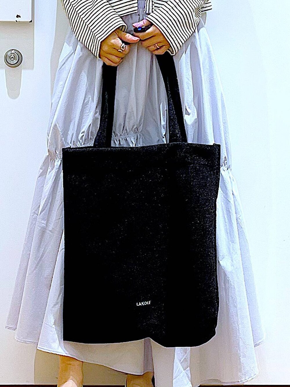 ブラック系のトートバッグ、ブルー系のスカート、イエロー系のニット/セーターを着用したレディースの春コーディネートの9枚目の写真