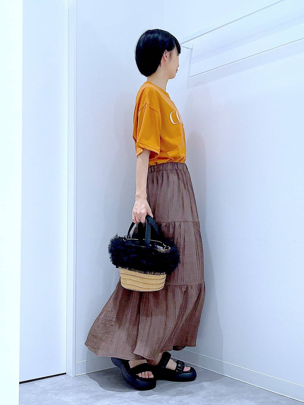 ベージュ系のショルダーバッグ、ブラック系のサンダル、オレンジ系のTシャツ/カットソーを着用したレディースの夏コーディネートの4枚目の写真