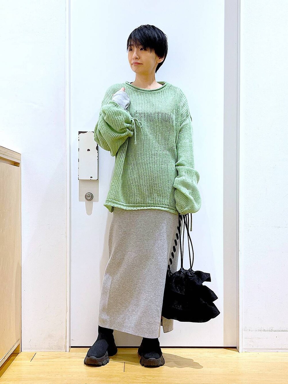 ブラック系のブーツ、グリーン系のニット/セーター、グレー系のスカートを着用したレディースの冬コーディネートの2枚目の写真