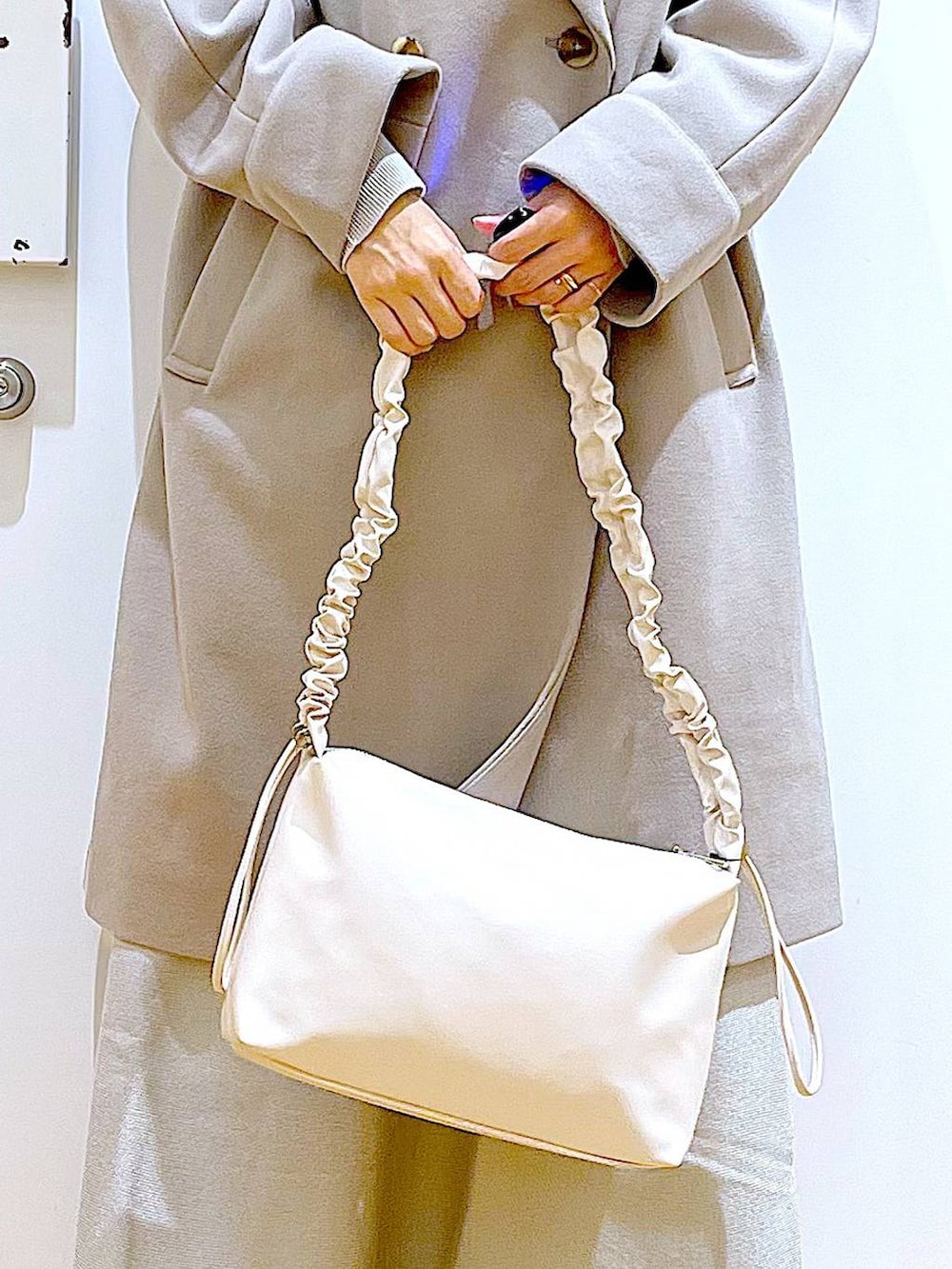 グレー系のステンカラーコート、ホワイト系のショルダーバッグ、グレー系のスカートを着用したレディースの冬コーディネートの9枚目の写真