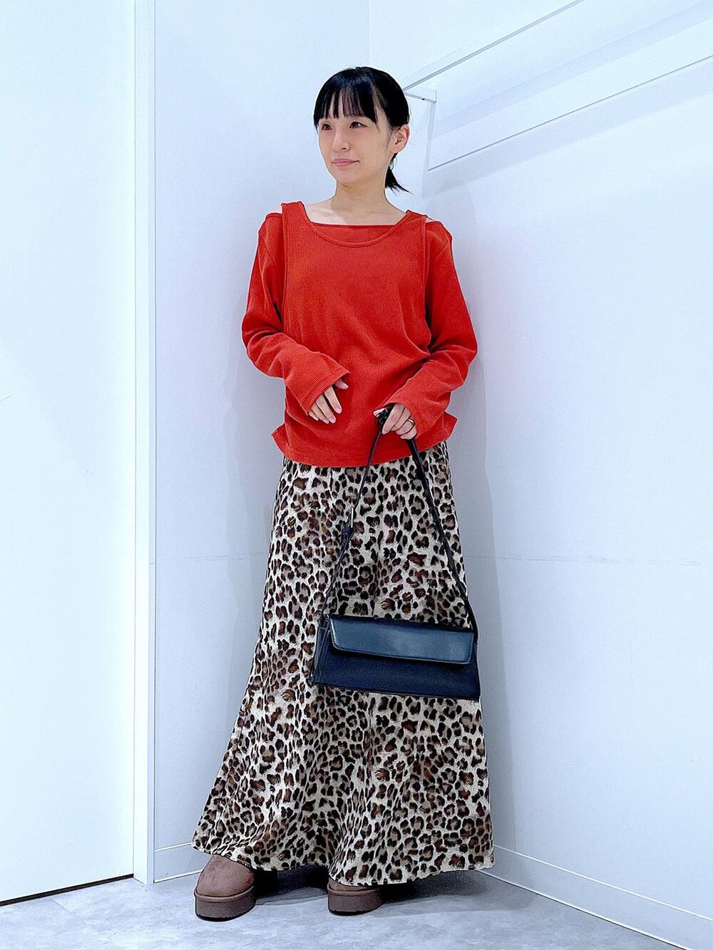 ブラック系のショルダーバッグ、ブラウン系のブーツ、ブラウン系のスカートを着用したレディースの秋コーディネートの2枚目の写真