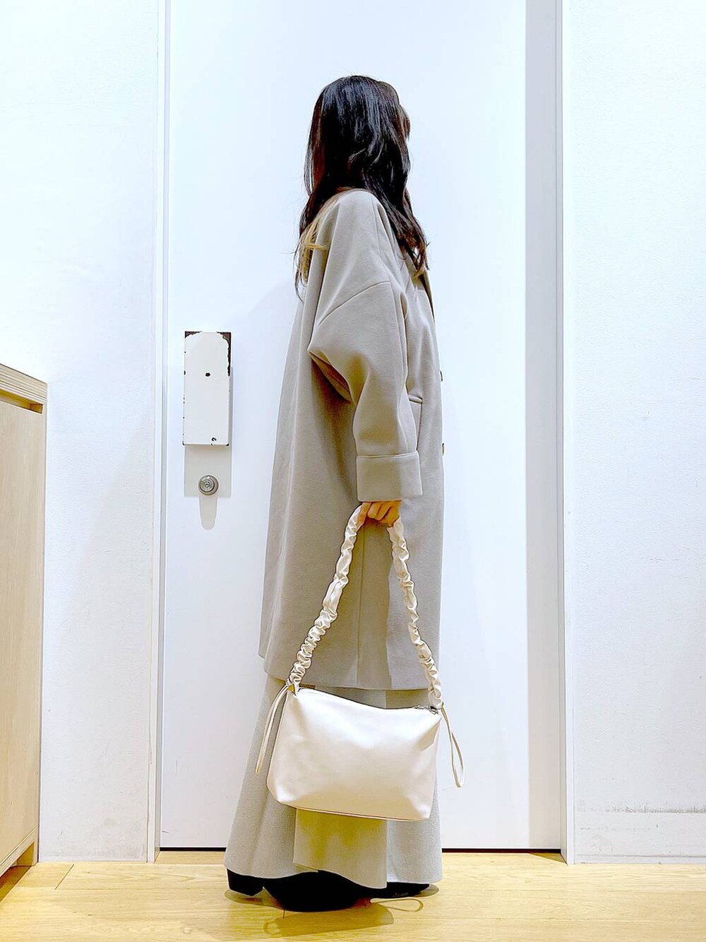 グレー系のステンカラーコート、ホワイト系のショルダーバッグ、グレー系のスカートを着用したレディースの冬コーディネートの4枚目の写真
