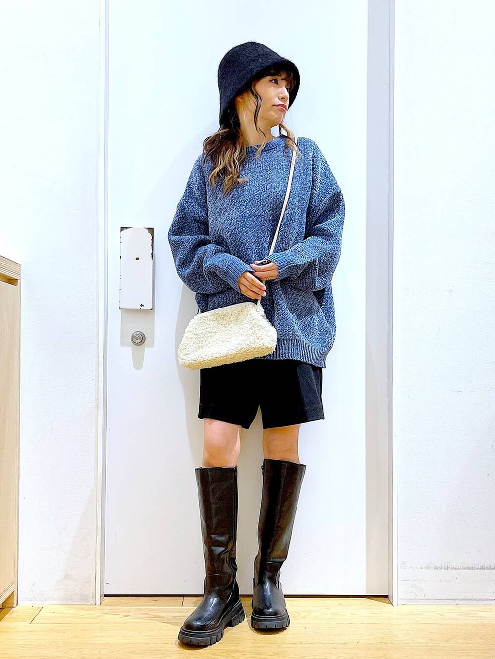 ブルー系のニット/セーター、ホワイト系のクラッチバッグ、ブラック系のブーツを着用したレディースの冬コーディネートの2枚目の写真