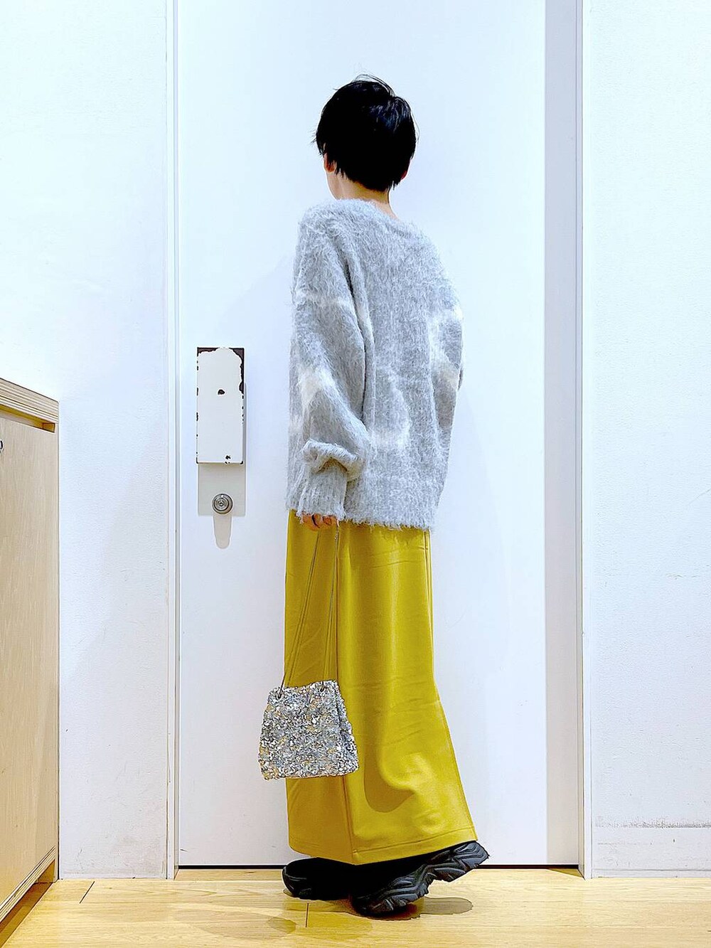 グレー系のニット/セーター、ブラック系のブーツ、イエロー系のスカートを着用したレディースの冬コーディネートの3枚目の写真