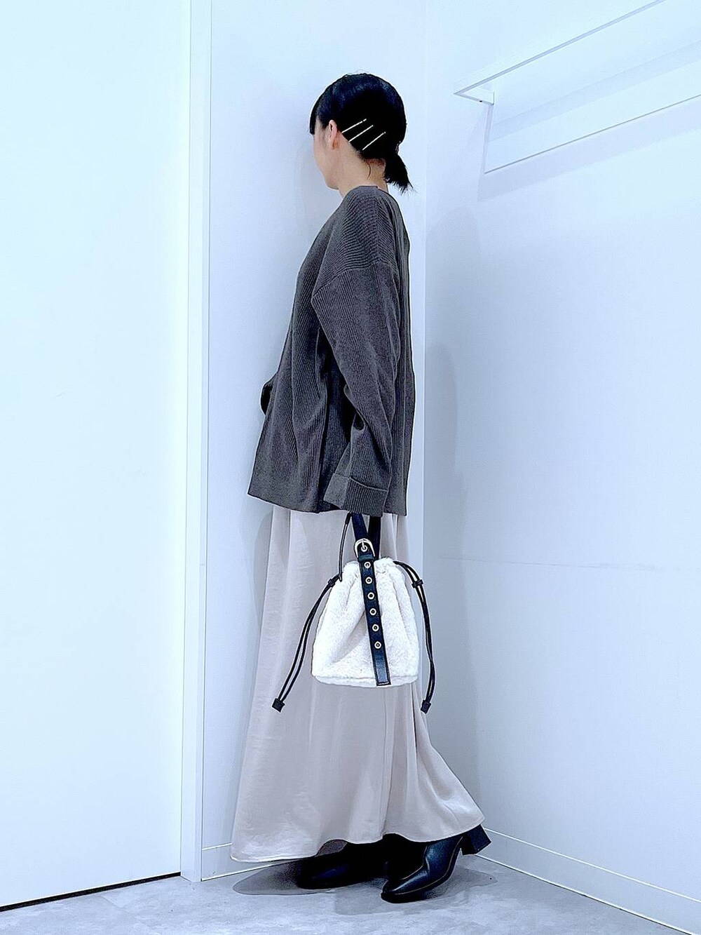 ホワイト系のハンドバッグ、ベージュ系のスカート、ブラック系のブーツを着用したレディースの秋コーディネートの3枚目の写真