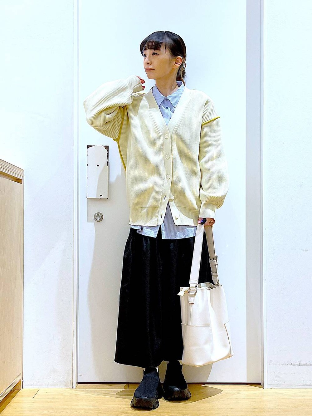 ホワイト系のショルダーバッグ、ホワイト系のカーディガン/ボレロ、ブラック系のスカートを着用したレディースの春コーディネートの2枚目の写真
