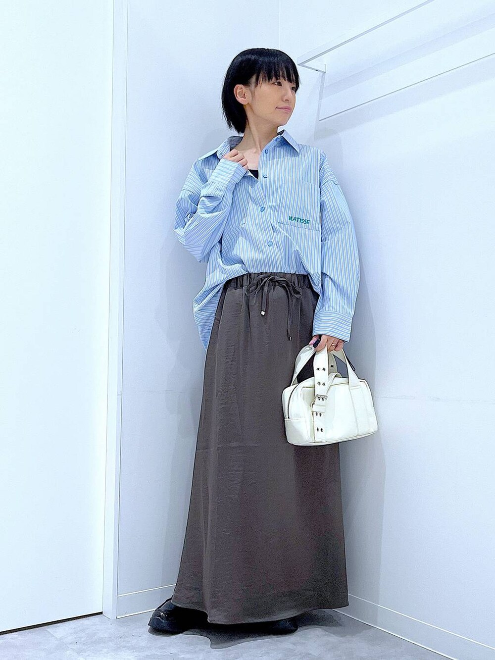 ブラック系のローファー、ホワイト系のショルダーバッグ、グレー系のスカートを着用したレディースの秋コーディネートの2枚目の写真