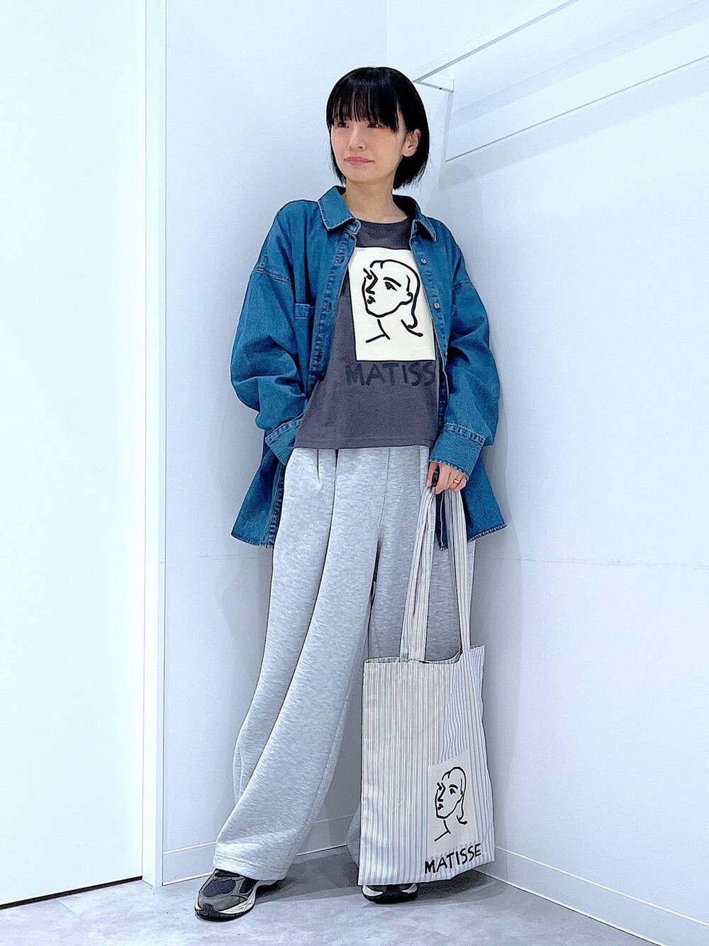 ブルー系のシャツ/ブラウス、ブラウン系のトートバッグ、グレー系のTシャツ/カットソーを着用したレディースの秋コーディネートの2枚目の写真