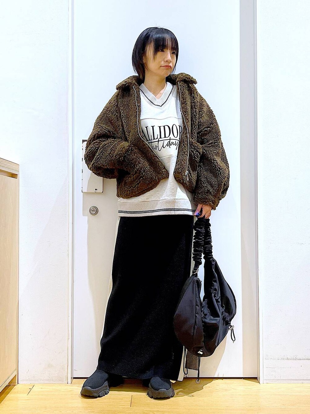 ブラック系のスカート、ブラック系のショルダーバッグ、ブラック系のブーツを着用したレディースの冬コーディネートの2枚目の写真