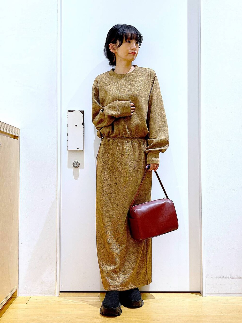 レッド系のショルダーバッグ、ブラック系のブーツ、ブラウン系のスウェットを着用したレディースの冬コーディネートの2枚目の写真