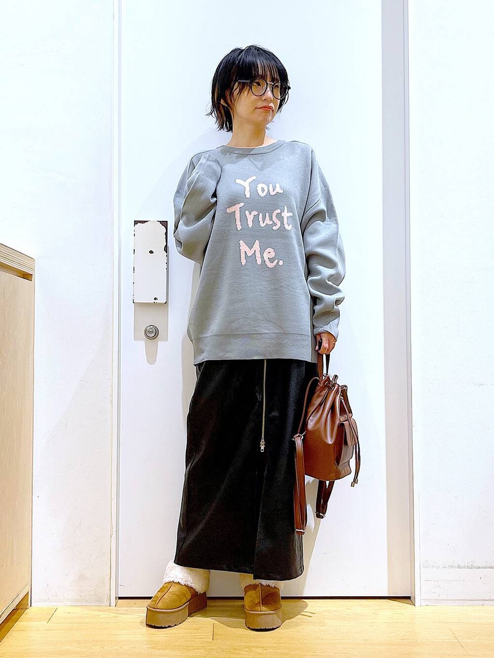 グレー系のニット/セーター、ブラウン系のバックパック/リュック、ブラック系のスカートを着用したレディースの冬コーディネートの2枚目の写真