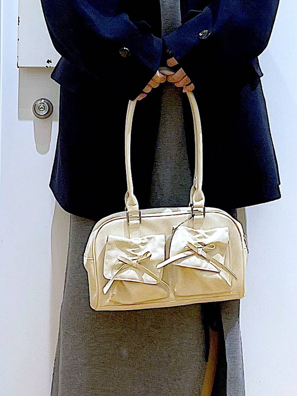 ブルー系のステンカラーコート、ホワイト系のハンドバッグ、ブラック系のブーツを着用したレディースの冬コーディネートの9枚目の写真