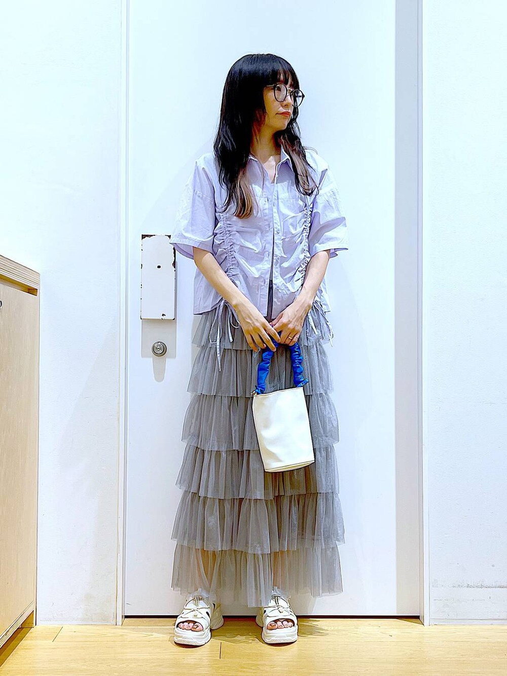ブルー系のショルダーバッグ、ホワイト系のサンダル、グレー系のスカートを着用したレディースの夏コーディネートの2枚目の写真