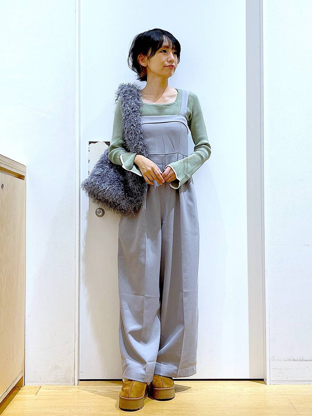グリーン系のニット/セーター、グレー系のサロペット/オーバーオール、グレー系のショルダーバッグを着用したレディースの秋コーディネートの2枚目の写真