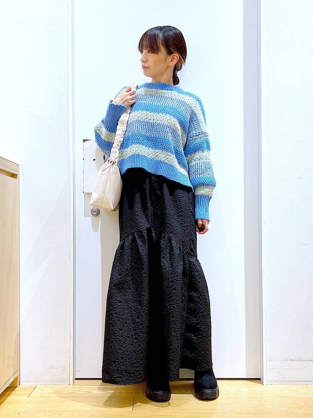 ホワイト系のショルダーバッグ、ブラック系のブーツ、ブラック系のスカートを着用したレディースの冬コーディネートの2枚目の写真