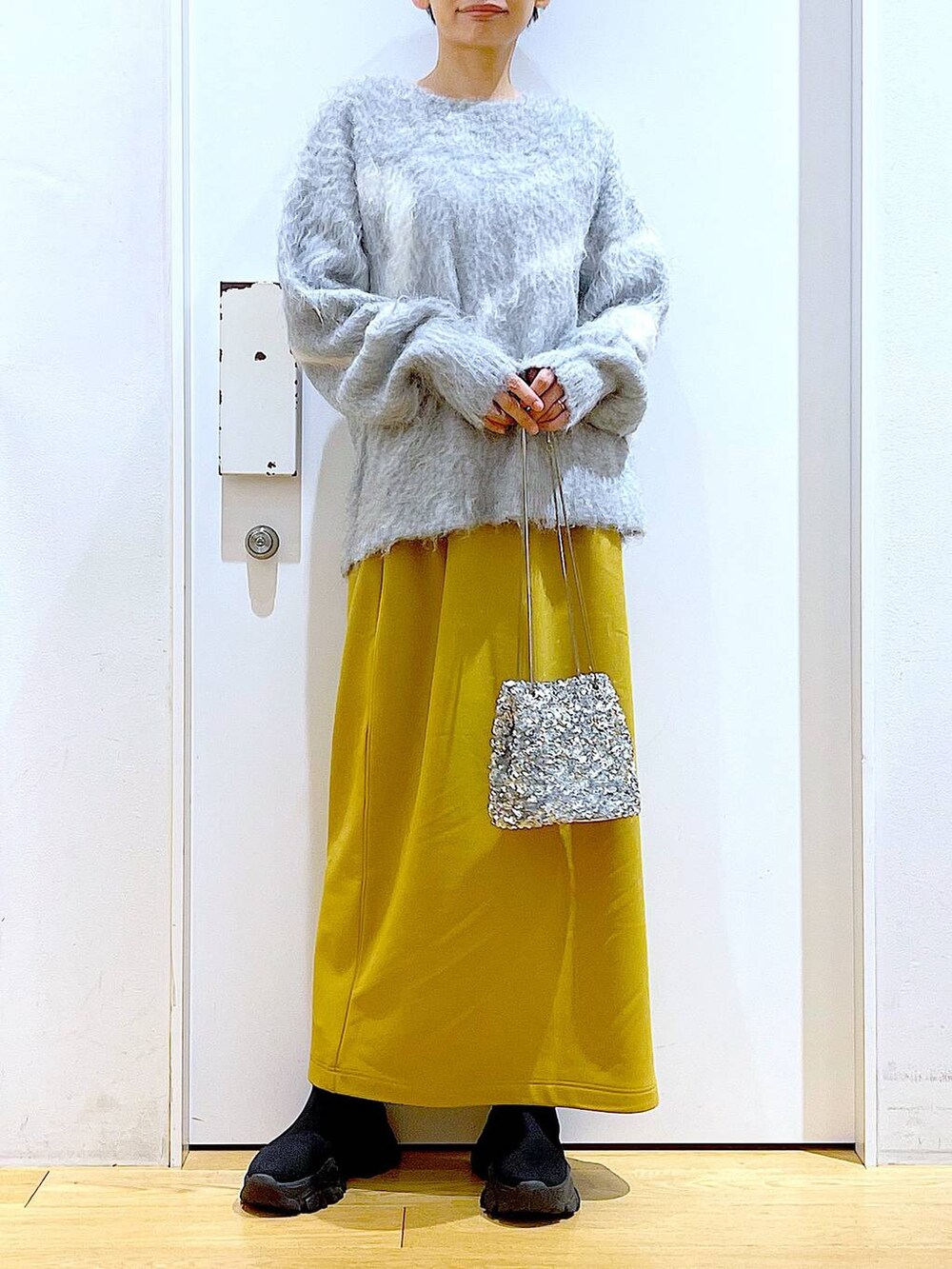 グレー系のニット/セーター、ブラック系のブーツ、イエロー系のスカートを着用したレディースの冬コーディネートの6枚目の写真