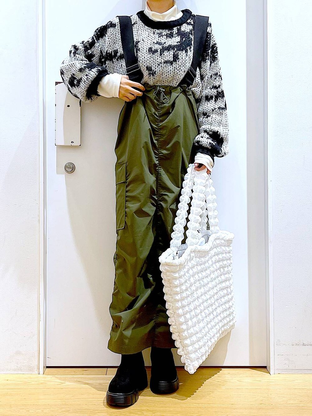 ホワイト系のトートバッグ、ベージュ系のTシャツ/カットソー、グリーン系のジャンパースカートを着用したレディースの冬コーディネートの6枚目の写真