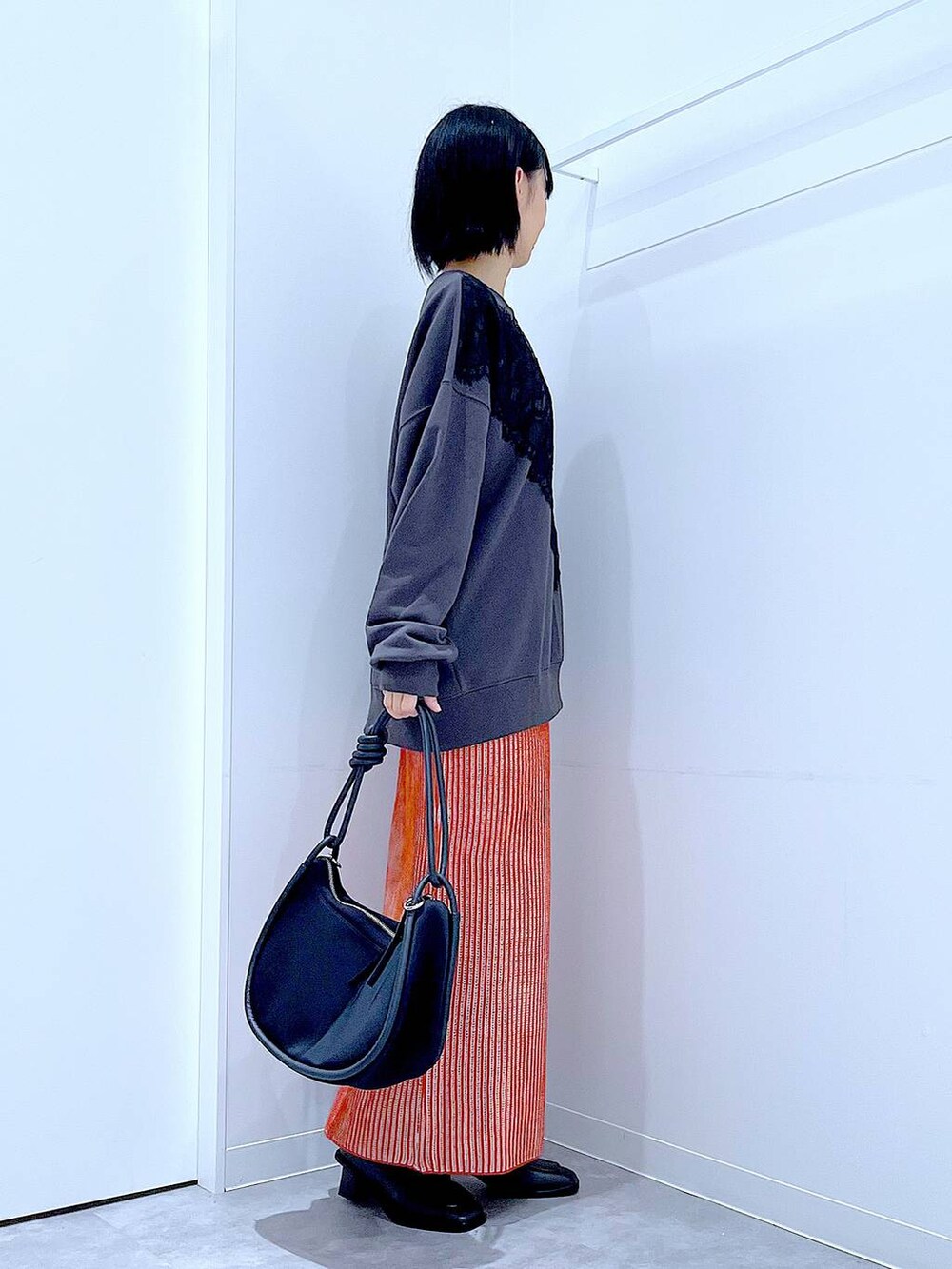 オレンジ系のスカート、ブラック系のブーツ、ブラック系のショルダーバッグを着用したレディースの秋コーディネートの4枚目の写真