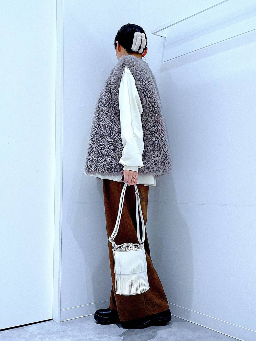 グレー系のベスト、ホワイト系のショルダーバッグ、ブラック系のブーツを着用したレディースの冬コーディネートの3枚目の写真