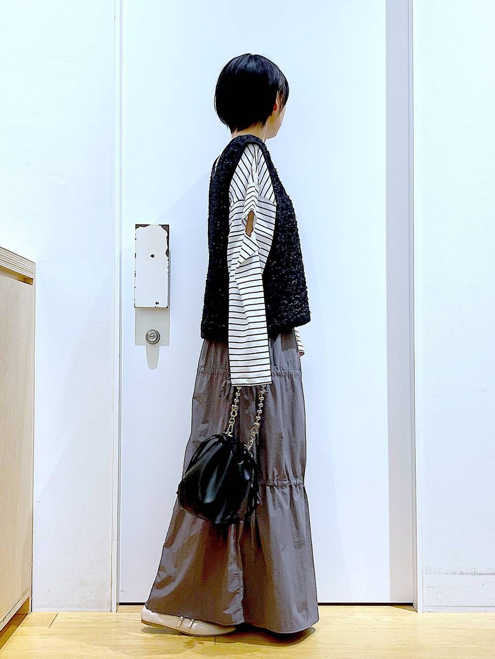 ブラック系のショルダーバッグ、ホワイト系のパンプス、グレー系のスカートを着用したレディースの秋コーディネートの4枚目の写真