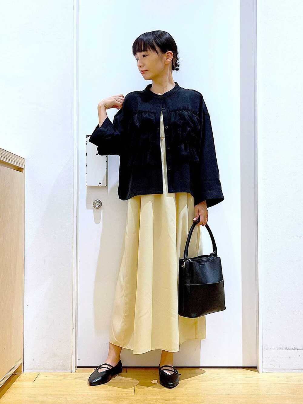 イエロー系のワンピース、ブラック系のショルダーバッグ、ブラック系のパンプスを着用したレディースの秋コーディネートの2枚目の写真