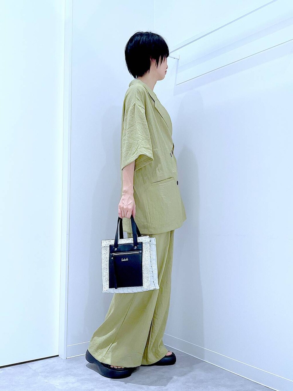 ホワイト系のショルダーバッグ、ブラック系のサンダル、グリーン系のテーラードジャケットを着用したレディースの夏コーディネートの4枚目の写真