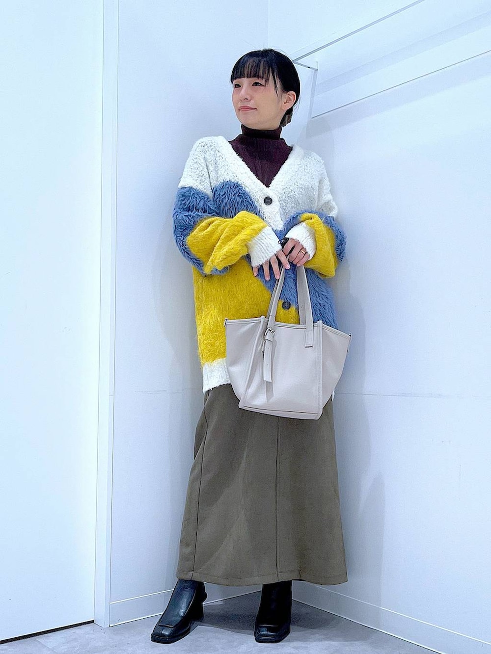 イエロー系のカーディガン/ボレロ、ブラック系のブーツ、グリーン系のスカートを着用したレディースの冬コーディネートの2枚目の写真