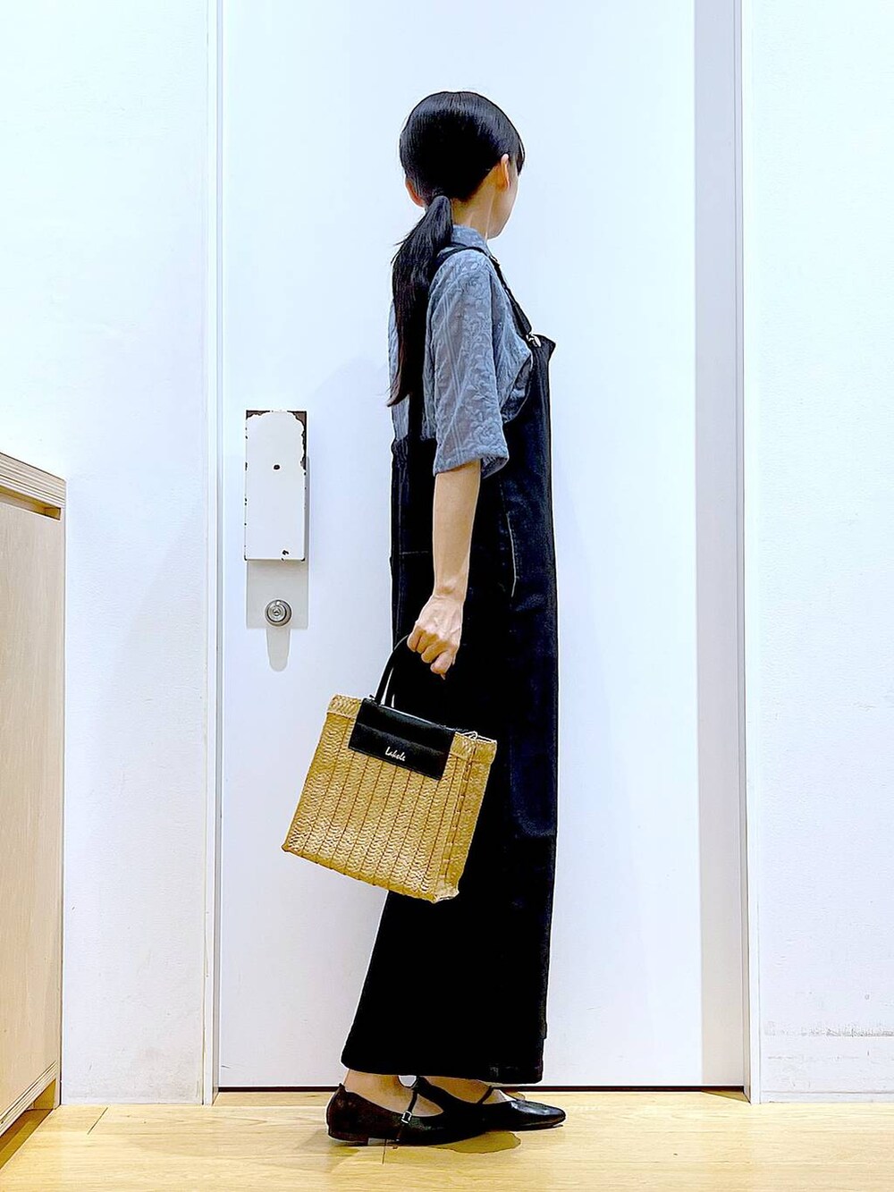 グレー系のジャンパースカート、ブラック系のパンプス、ベージュ系のショルダーバッグを着用したレディースの夏コーディネートの4枚目の写真