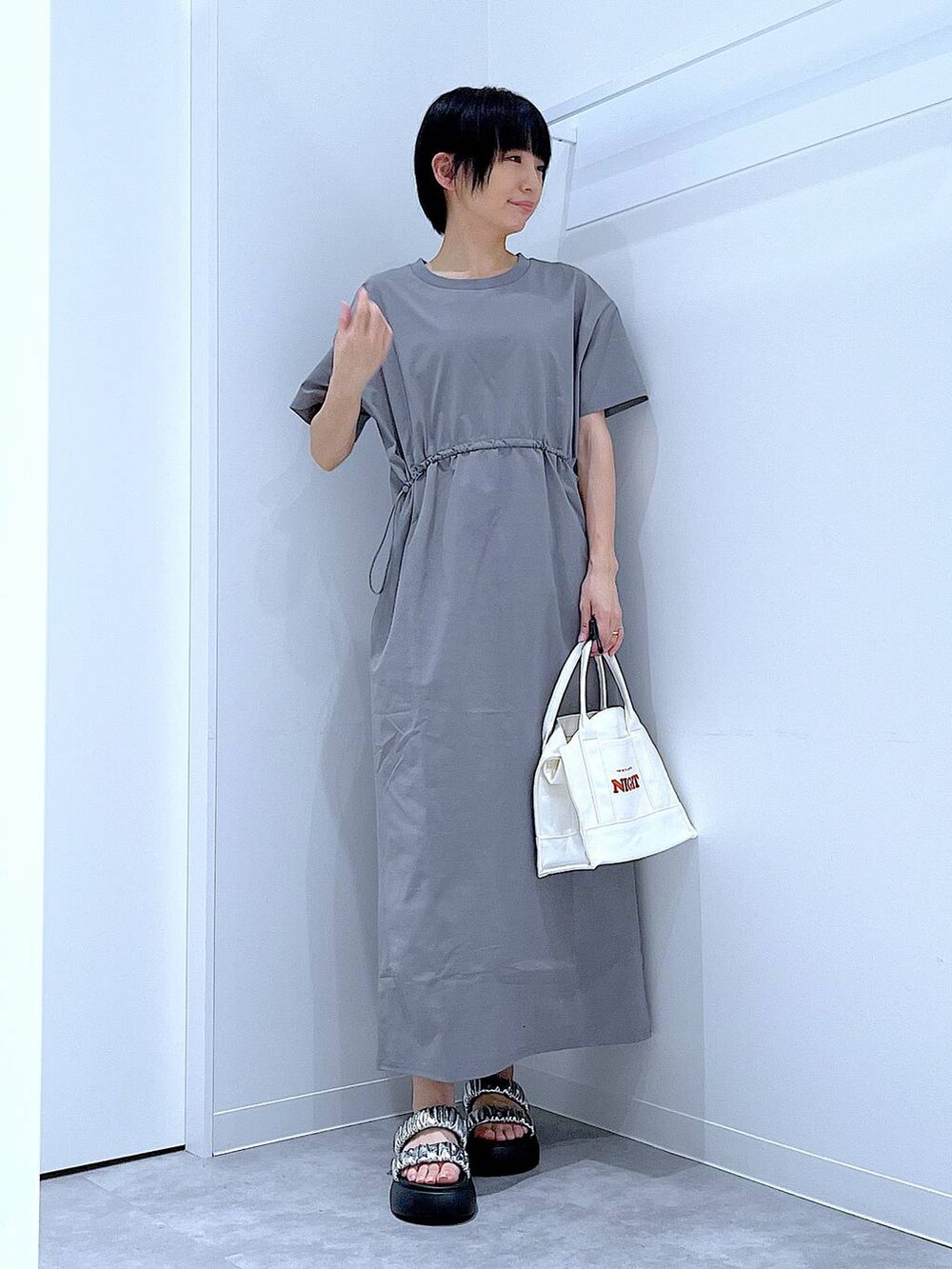 シルバー系のサンダル、グレー系のワンピース、ホワイト系のトートバッグを着用したレディースの夏コーディネートの2枚目の写真