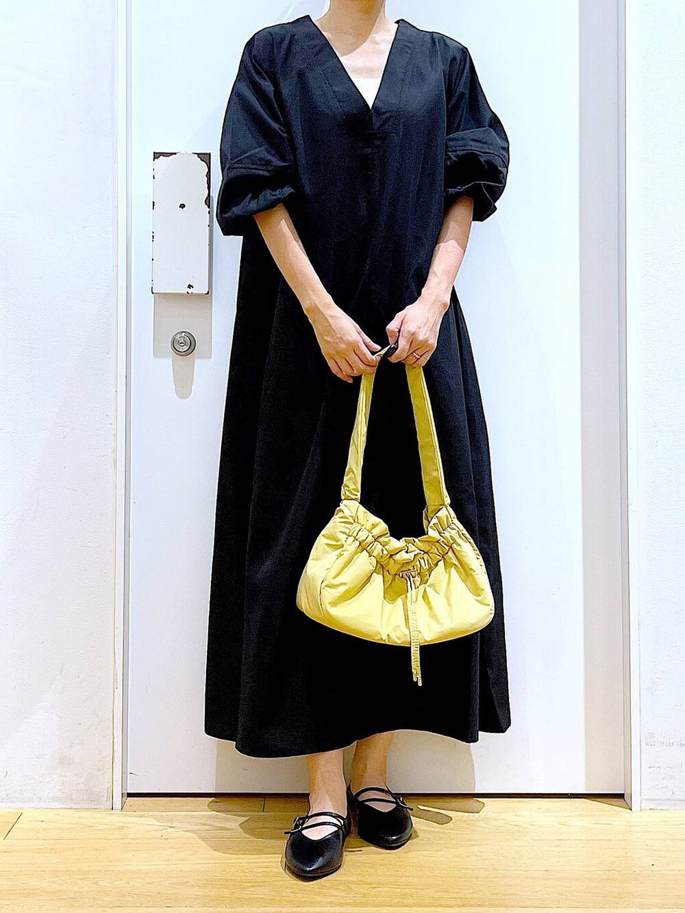 イエロー系のハンドバッグ、ブラック系のワンピース、ブラック系のパンプスを着用したレディースの秋コーディネートの6枚目の写真