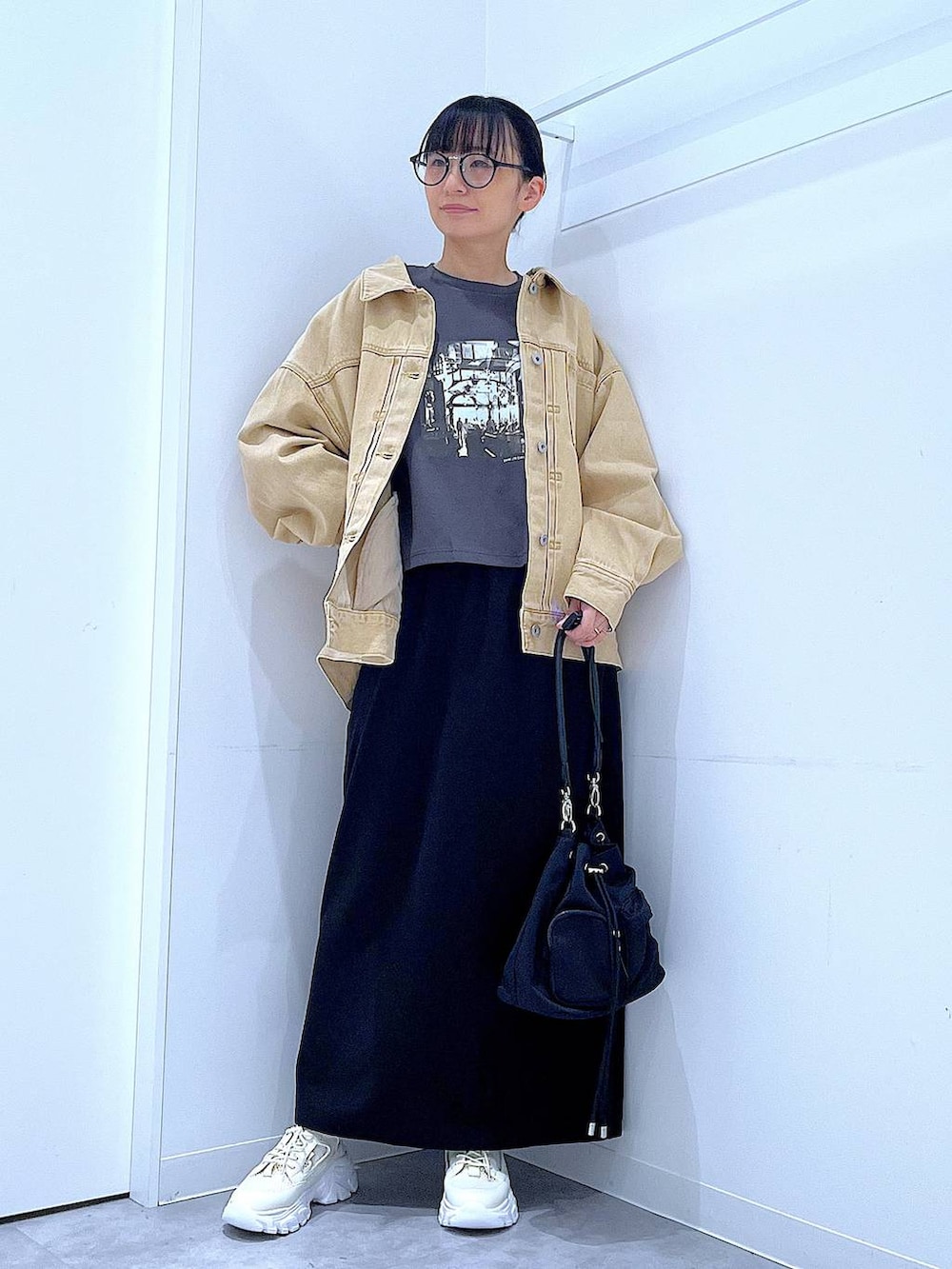 ブラック系のスカート、ベージュ系のデニムジャケット、ブラック系のショルダーバッグを着用したレディースの春コーディネートの2枚目の写真