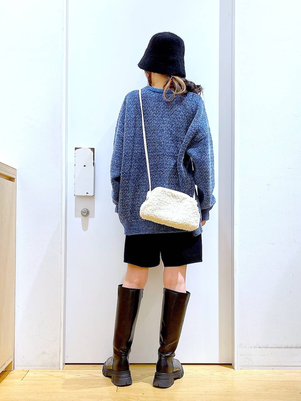 ブルー系のニット/セーター、ホワイト系のクラッチバッグ、ブラック系のブーツを着用したレディースの冬コーディネートの5枚目の写真