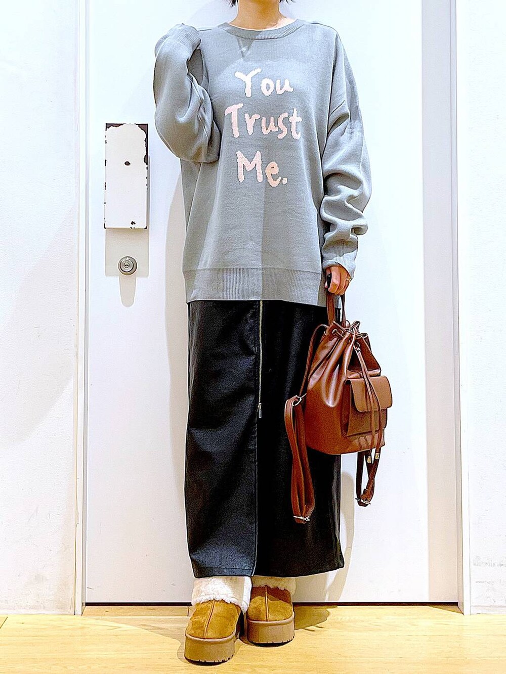 グレー系のニット/セーター、ブラウン系のバックパック/リュック、ブラック系のスカートを着用したレディースの冬コーディネートの6枚目の写真