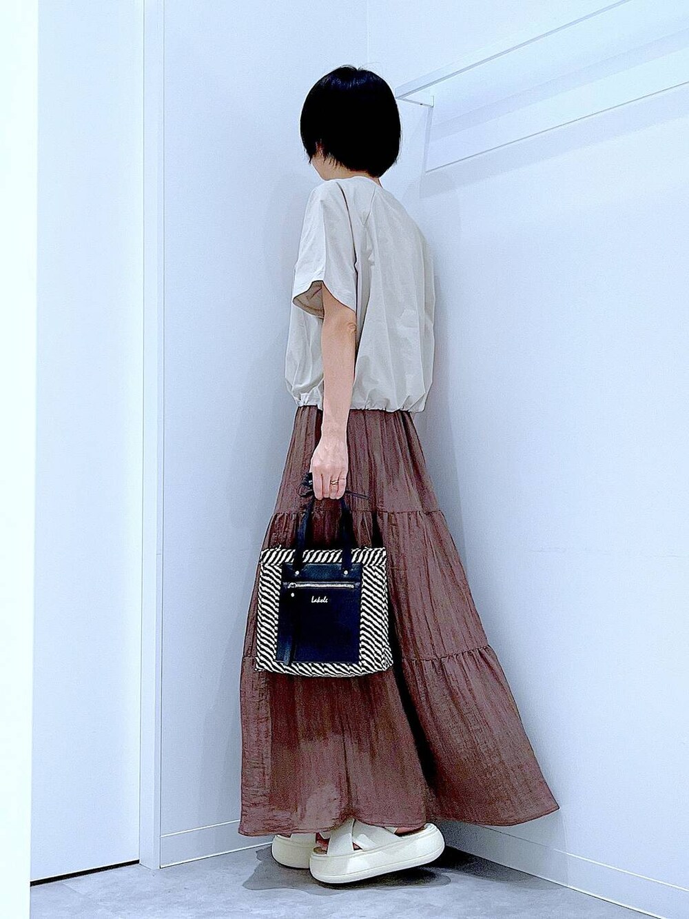 ブラック系のショルダーバッグ、ホワイト系のサンダル、ベージュ系のTシャツ/カットソーを着用したレディースの夏コーディネートの3枚目の写真