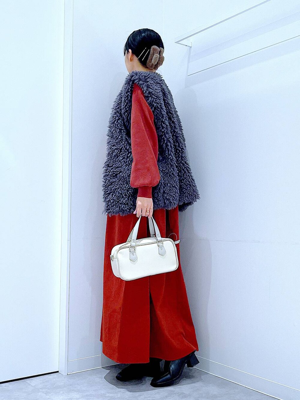 グレー系のベスト、ブラック系のブーツ、ホワイト系のショルダーバッグを着用したレディースの秋コーディネートの3枚目の写真