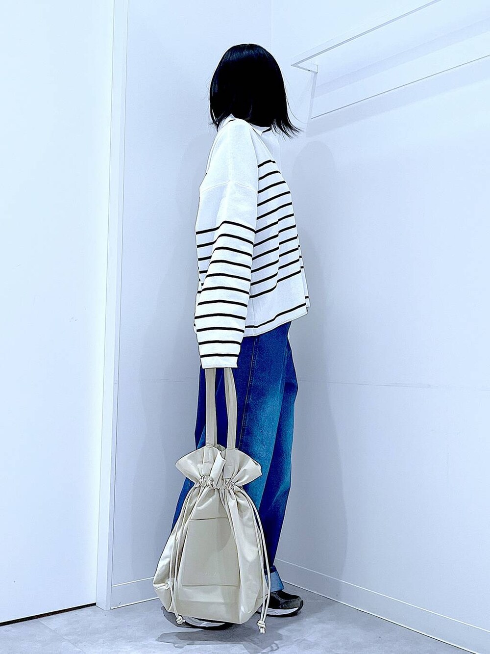 ブラック系のTシャツ/カットソー、ベージュ系のトートバッグ、ブルー系のデニムパンツを着用したレディースの冬コーディネートの4枚目の写真