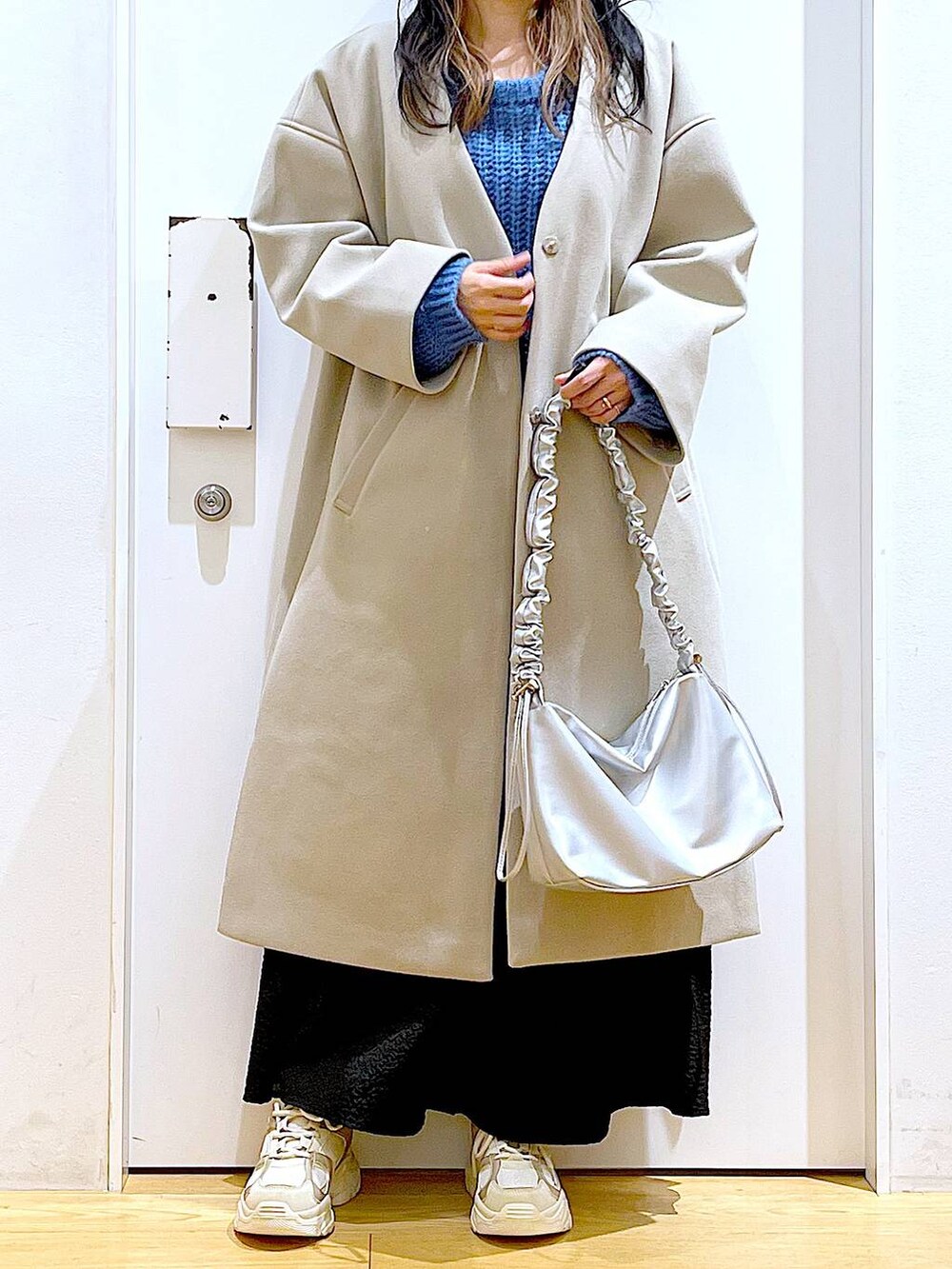 シルバー系のショルダーバッグ、ベージュ系のスニーカー、ベージュ系のノーカラーコートを着用したレディースの冬コーディネートの6枚目の写真