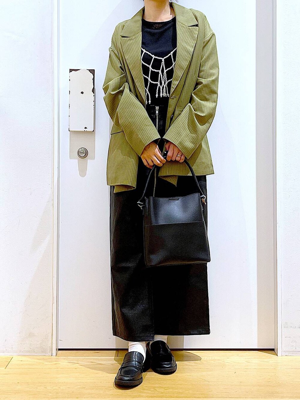 ホワイト系のベスト、ブラック系のスカート、ブラック系のショルダーバッグを着用したレディースの秋コーディネートの6枚目の写真
