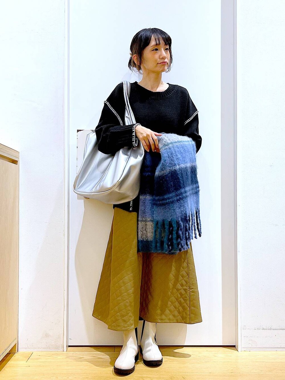 シルバー系のトートバッグ、ベージュ系のブーツ、ブラック系のニット/セーターを着用したレディースの冬コーディネートの2枚目の写真