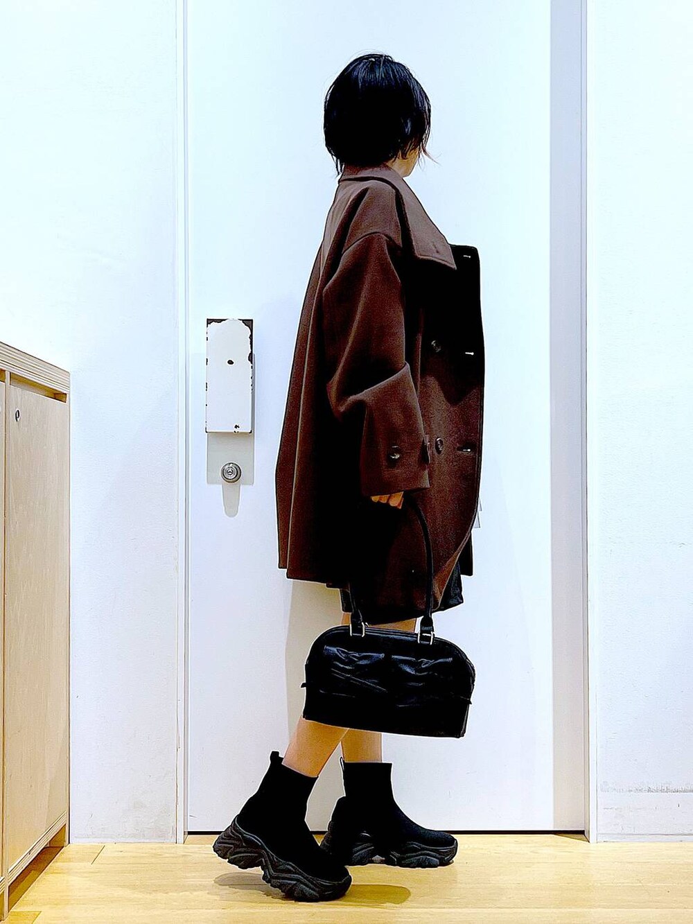 ブラウン系のステンカラーコート、ブラック系のハンドバッグ、ブラック系のブーツを着用したレディースの冬コーディネートの4枚目の写真