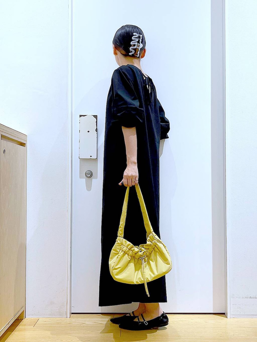 イエロー系のハンドバッグ、ブラック系のワンピース、ブラック系のパンプスを着用したレディースの秋コーディネートの3枚目の写真