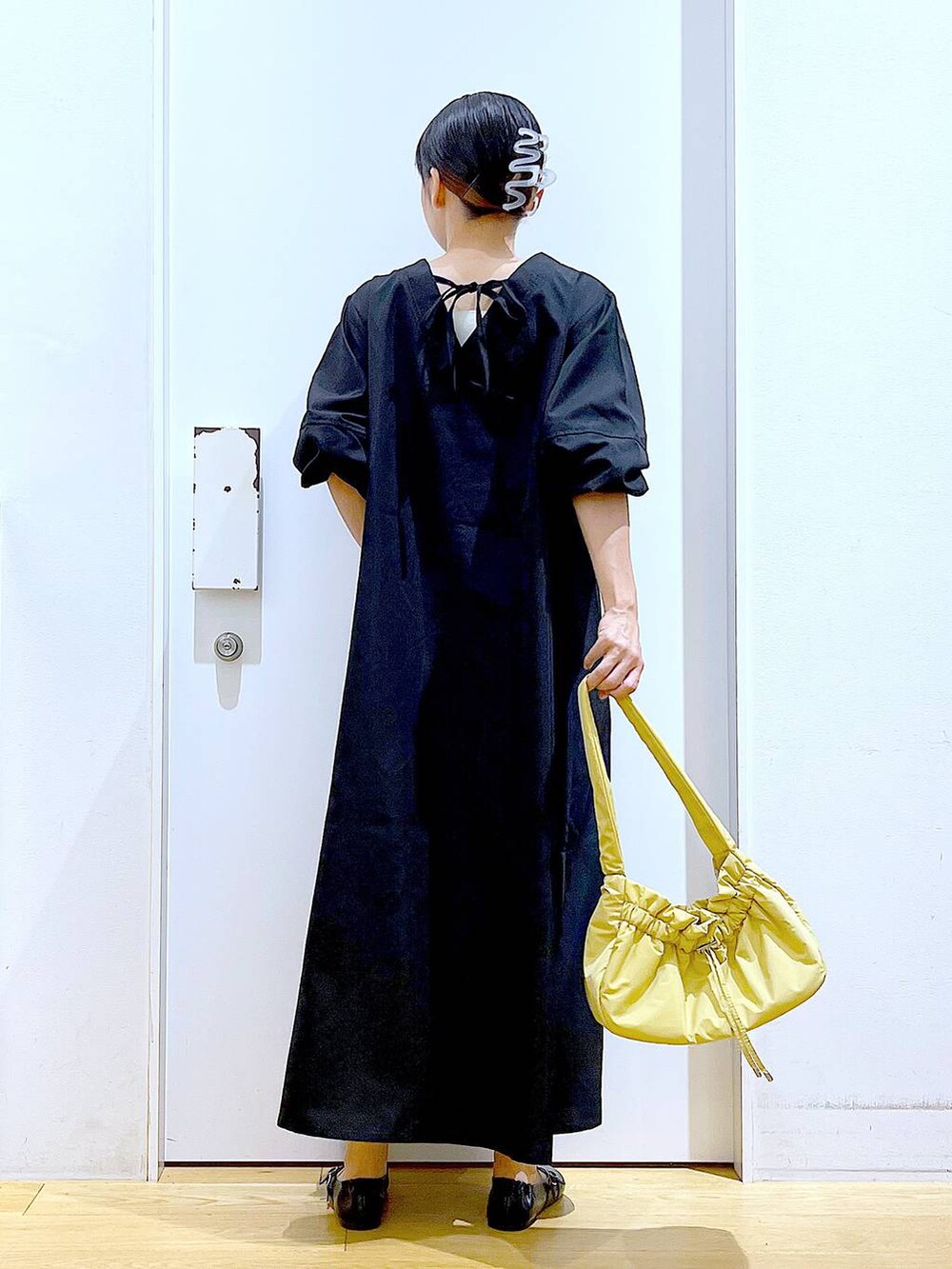 イエロー系のハンドバッグ、ブラック系のワンピース、ブラック系のパンプスを着用したレディースの秋コーディネートの5枚目の写真