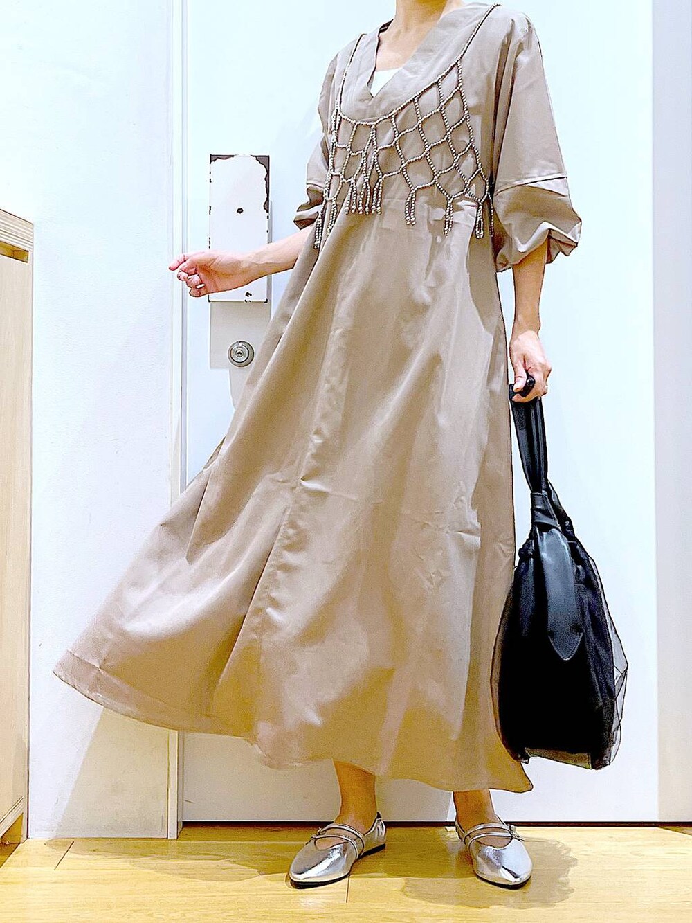 ブラック系のトートバッグ、ベージュ系のワンピース、シルバー系のパンプスを着用したレディースの夏コーディネートの6枚目の写真