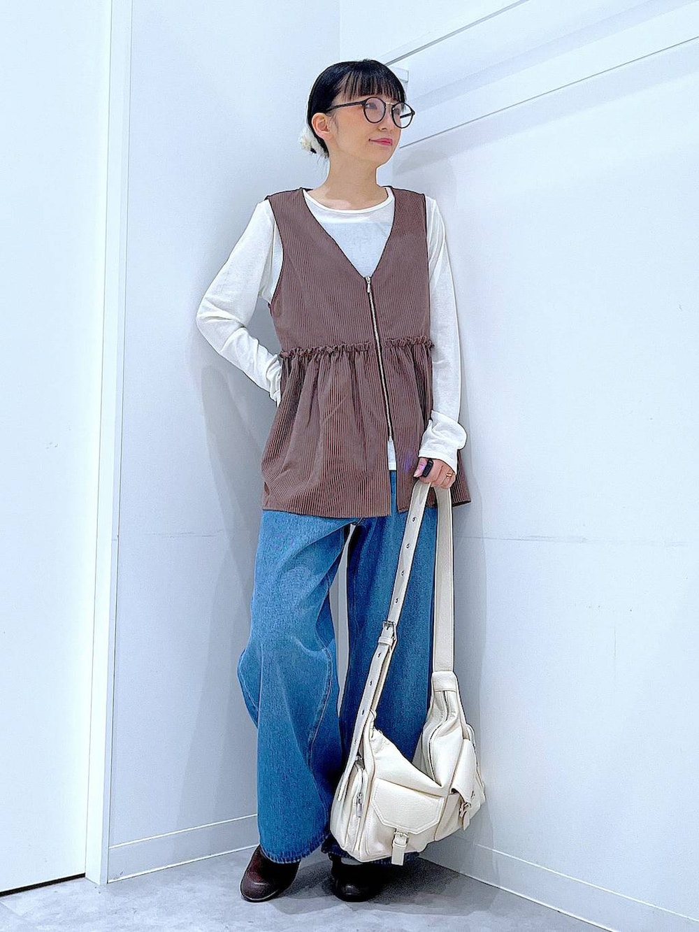 ブルー系のデニムパンツ、ブラウン系のベスト、ホワイト系のTシャツ/カットソーを着用したレディースの秋コーディネートの2枚目の写真