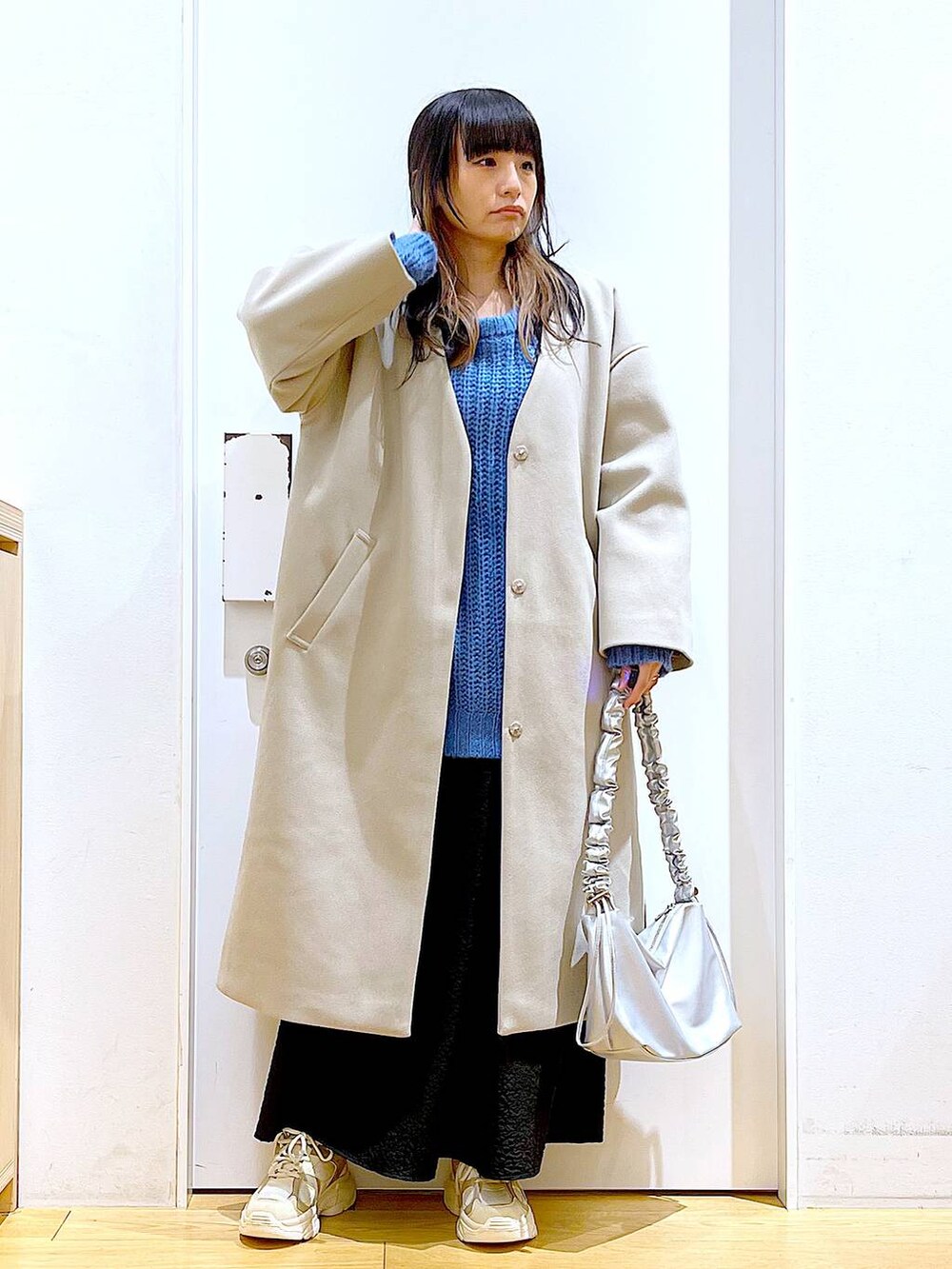 シルバー系のショルダーバッグ、ベージュ系のスニーカー、ベージュ系のノーカラーコートを着用したレディースの冬コーディネートの2枚目の写真