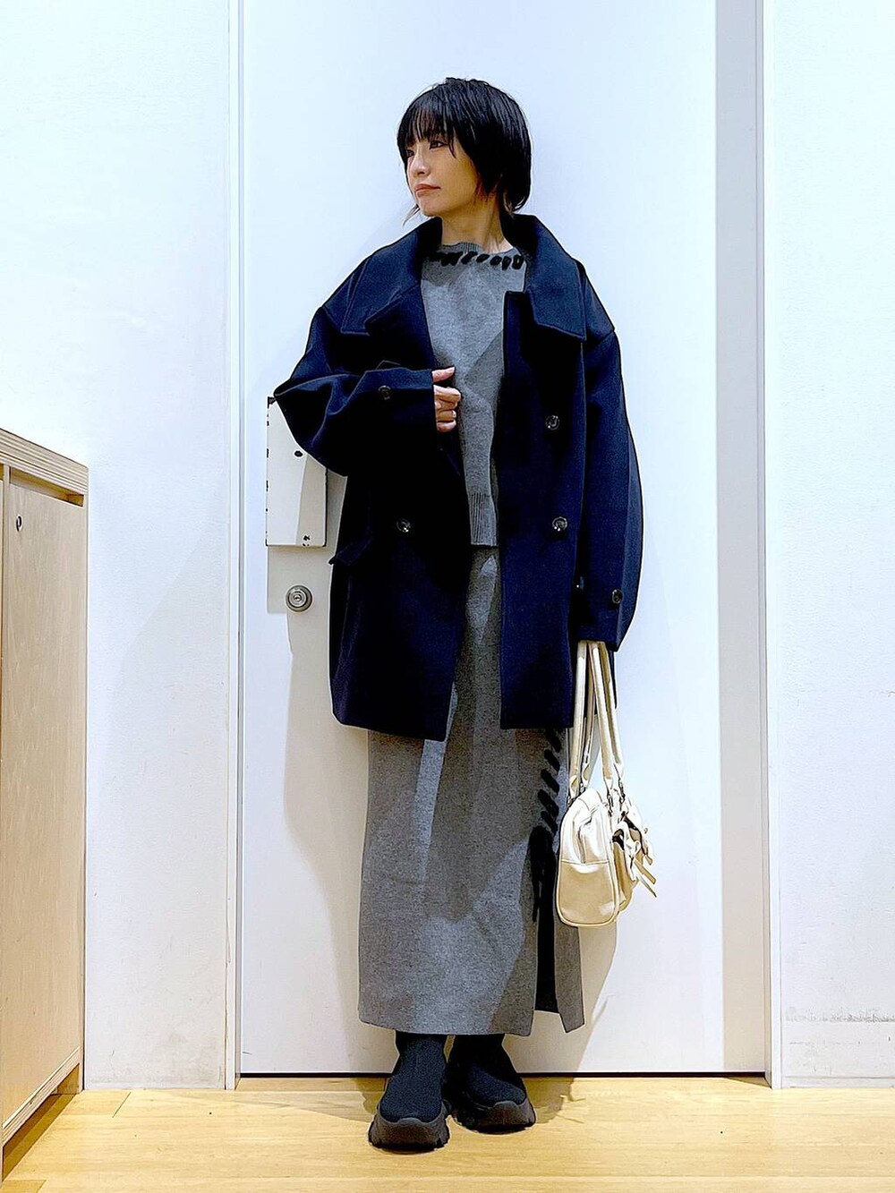 ブルー系のステンカラーコート、ホワイト系のハンドバッグ、ブラック系のブーツを着用したレディースの冬コーディネートの2枚目の写真